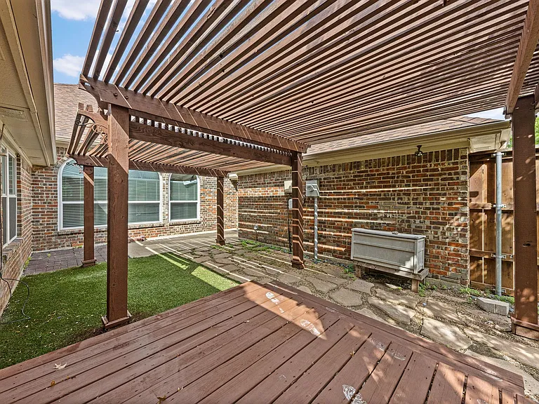 Covered pergola patio with paver seating area and private fenced yard access, ideal for outdoor dining or relaxing.