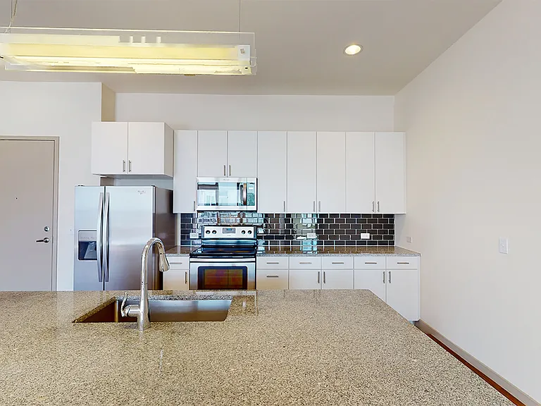 Apartment kitchen with stainless steel appliances, granite countertops and wood-style flooring.