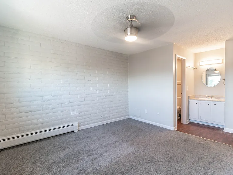 Bright and cozy bedroom with soft carpet flooring, modern ceiling fan, and an elegant vanity area exuding comfort and style.