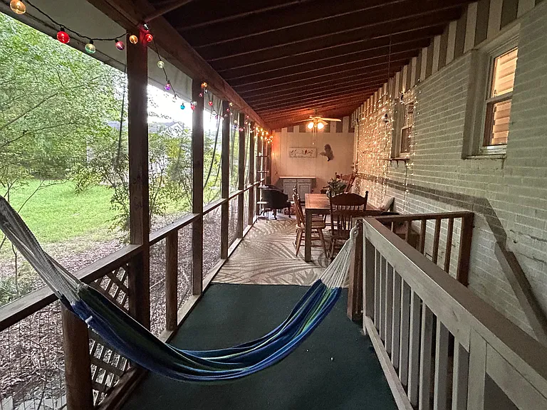 Covered screened porch with ceiling fan, string lights, and space for dining or relaxing while enjoying yard views.