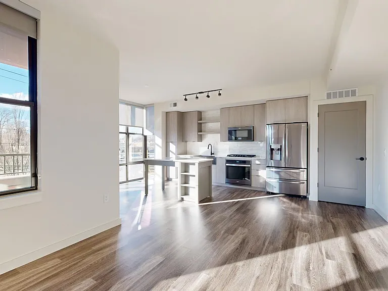 Apartment kitchen with black stainless steel appliances, dining and living room with wood-style flooring.