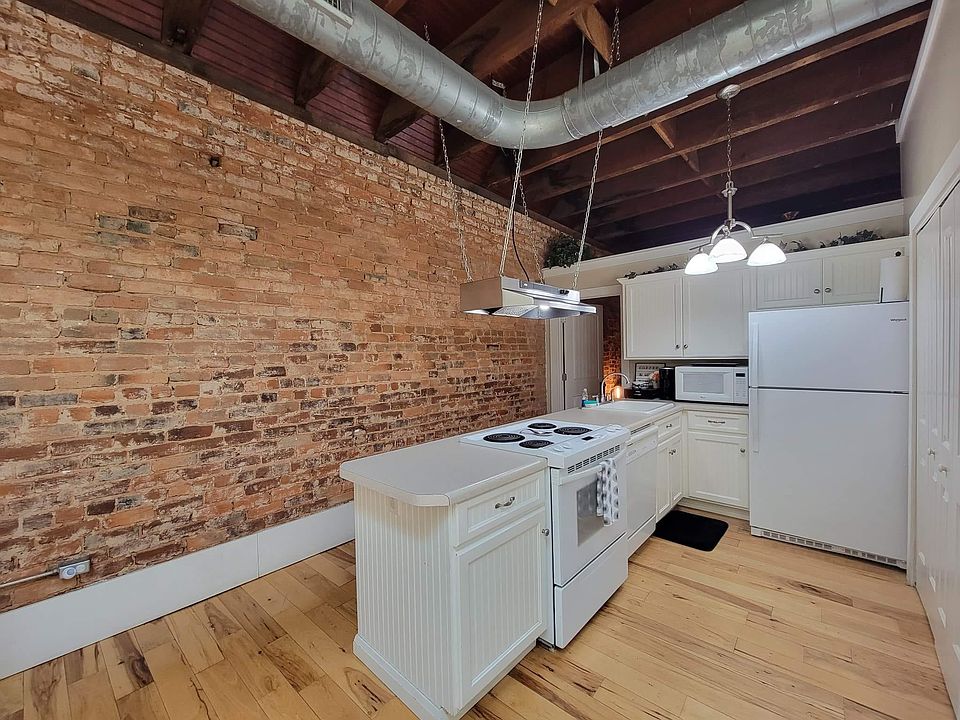 Open concept galley kitchen with exposed brick wall and appliances.