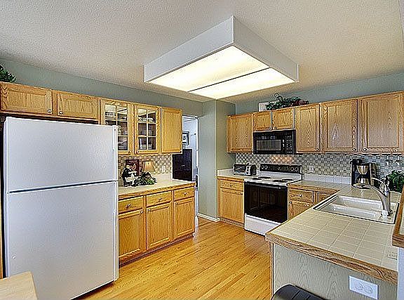 Open country kitchen w/ oak floors & cabinets, pantry, & tile counters.