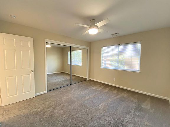 Large bedroom with ceiling fan and mirrored closet doors.