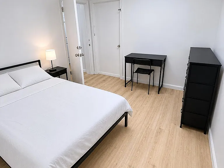 Furnished bedroom with a full bed, nightstand with lamp, dedicated desk, and dresser on wood-look flooring.