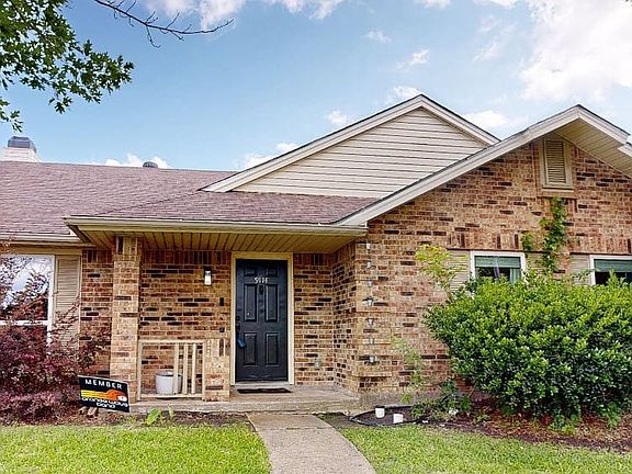 Brick facade residence featuring a covered front entry, dark paneled front door, and mature landscaping