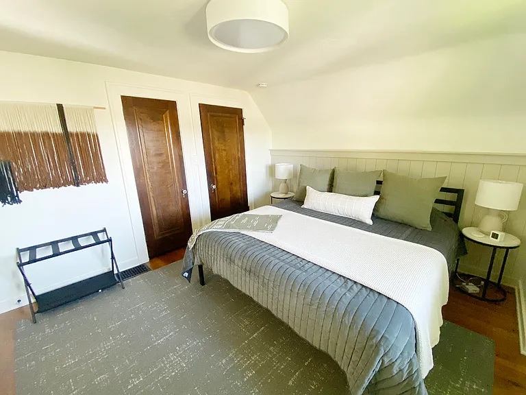 The second upstairs bedroom features a king bed with plush bedding, a dedicated workspace, and a twin fold-out mattress tucked away in one of two closets. A full bathroom with a tiled walk-in shower is just steps away.