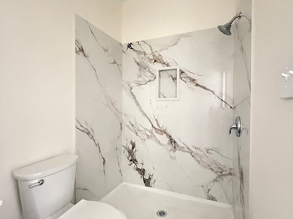 Bathroom _ Elegant and modern design featuring full granite-style walls in the shower, a sleek vanity with matching countertop, premium fixtures, and rich wood-look flooring for a warm, upscale finish.
