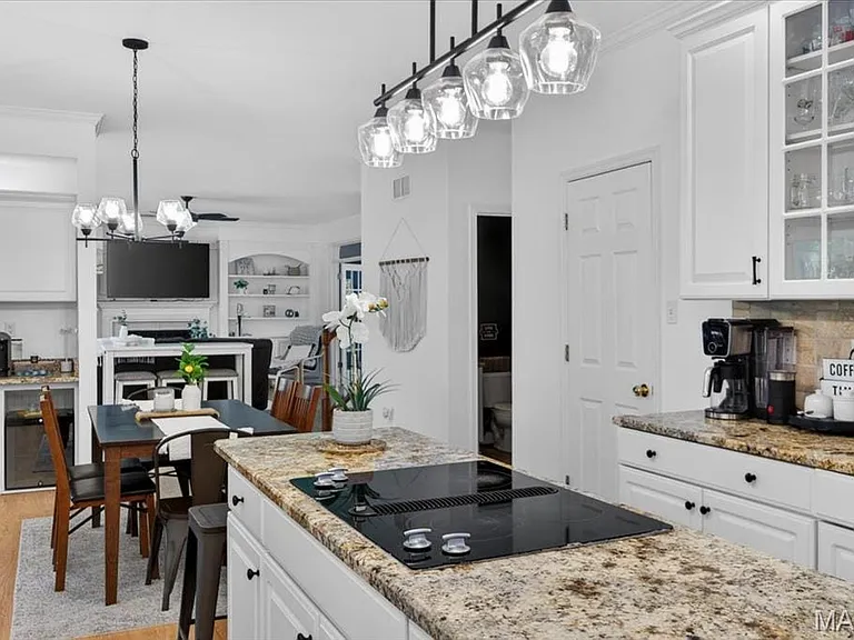 Kitchen featuring a spacious island with an integrated cooktop, stone countertops, white cabinetry with dark hardware, and a tile backsplash