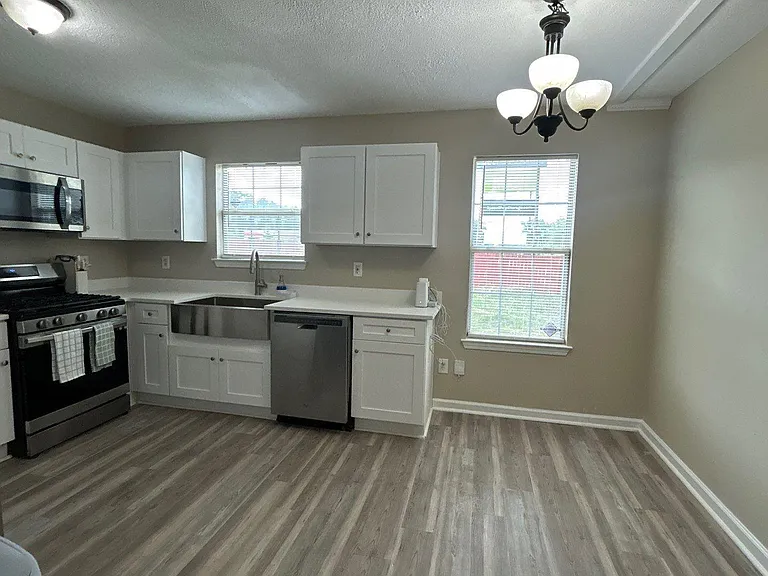 Open kitchen with white cabinets, stainless appliances, and generous counter space beside two windows for everyday dining.