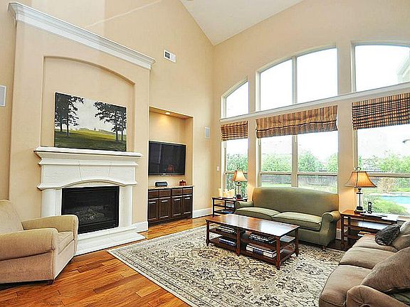 Family Room with  two story ceiling and  beautiful hardwoods. Built in entertainment center. Stone fireplace  with custom mantel. Arched windows with woven woods.