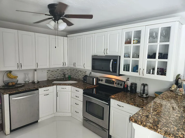 U-shaped kitchen with ample white cabinetry, granite-look counters, mosaic backsplash, and stainless range, microwave, and di