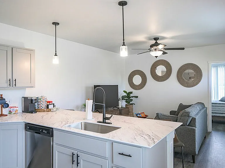 Elegant modern living space featuring open-concept kitchen with marble countertops, cozy living area, stylish decor, and view into a bright bedroom.
