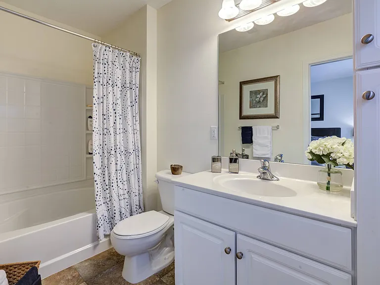 Bright white bathroom with white vanity and built-in linen closet. Oversized mirror hung above vanity with toilet and shower to the left at Summit Place apartments in Methuen, MA.
