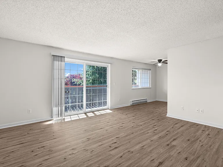Bright and airy living room with stylish wood flooring, large windows, and a sliding glass door to a sunlit balcony.