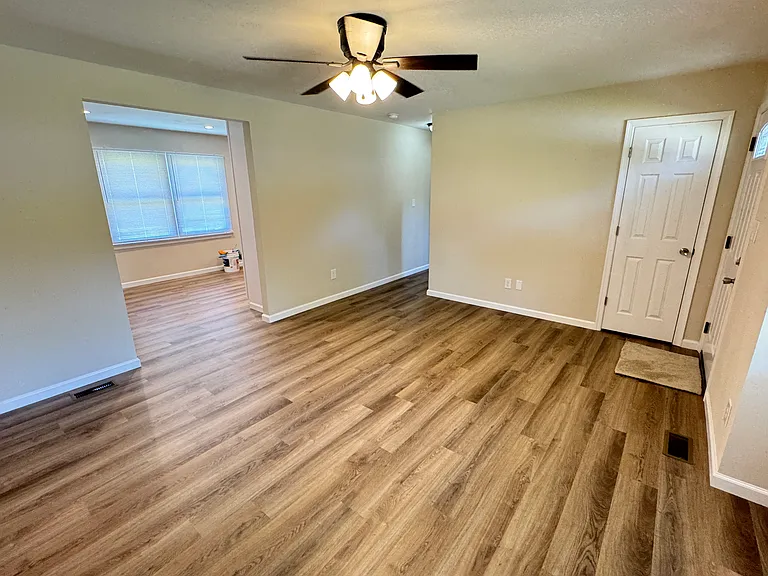 Living room looking into kitchen and down hall. Front door is on the right. Coat closet is straight ahead.