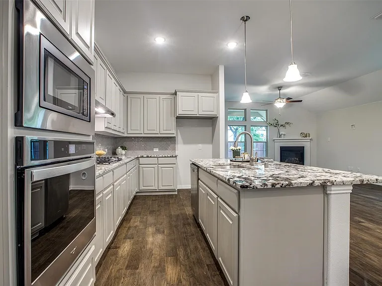 Contemporary kitchen featuring light-toned cabinetry, stainless steel built-in appliances, wood-finish flooring, and a speckled countertop island with an undermount sink and pendant lighting