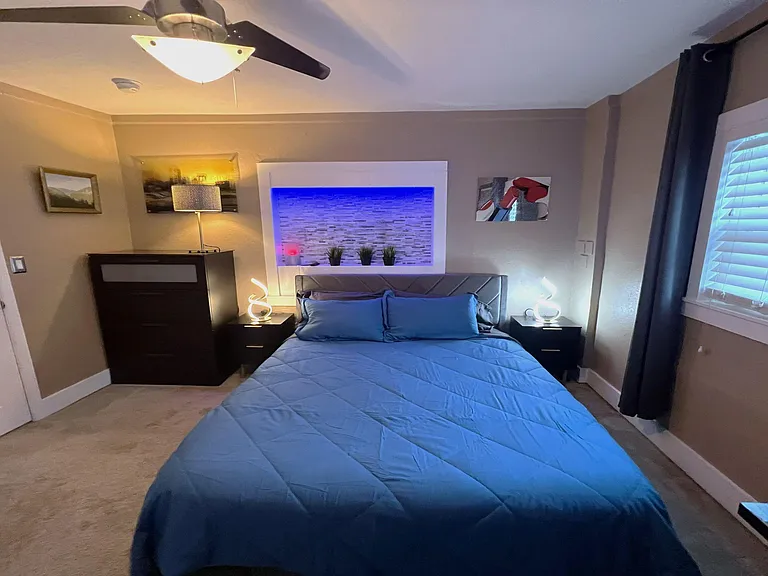 Furnished bedroom with a queen bed, nightstands, and a decorative headboard alcove plus a window with curtains.