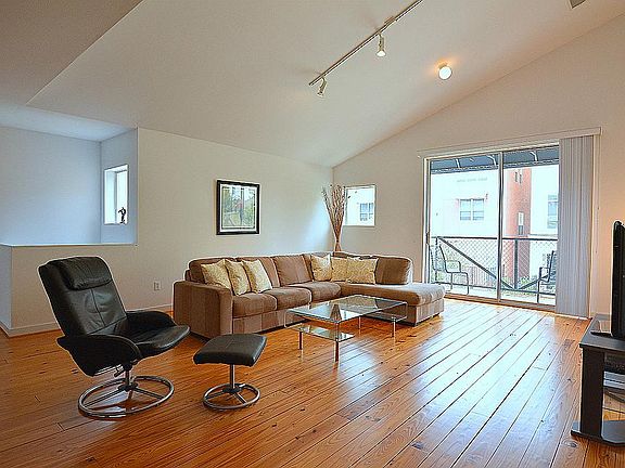 View of the living area with pine flooring, hight ceiling wall of windows that allow the room to be 