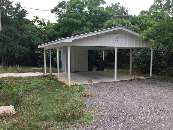 Two vehicle carport with storage room, small concrete patio visible to the left