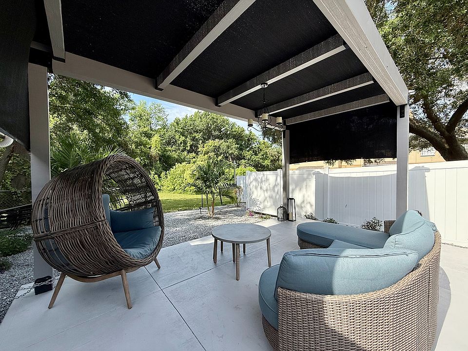 Charming patio with modern wicker furniture, featuring a cozy hanging chair and stylish seating, surrounded by lush greenery and shaded by an elegant canopy.