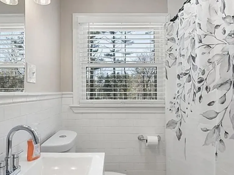 Full bath with tiled tub/shower, single-sink vanity, and a window with blinds for ventilation and natural light.
