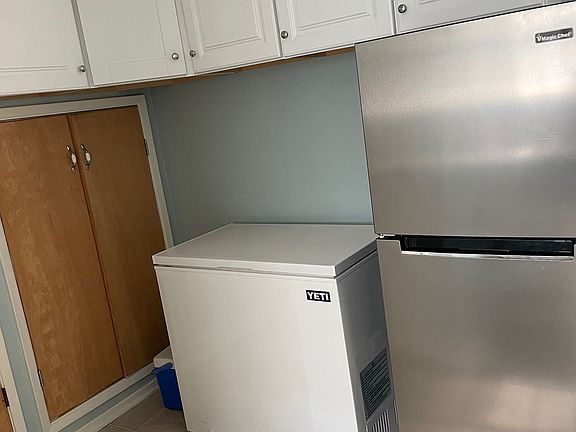 Several upper kitchen cabinets and closet or pantry space underneath behind wooden doors, deep freezer not included