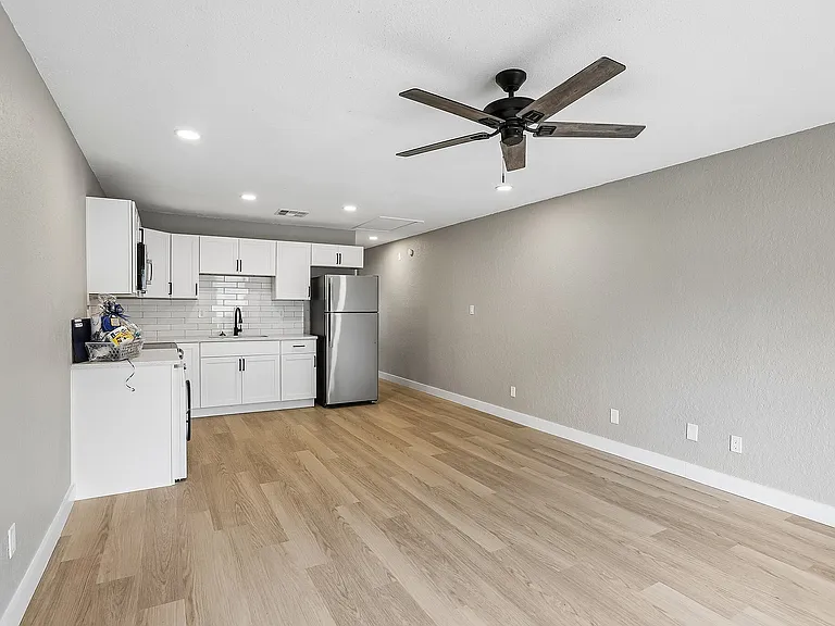 Modern open-concept apartment featuring a sleek kitchen with white cabinetry, stainless steel appliances, and elegant hardwood floors.