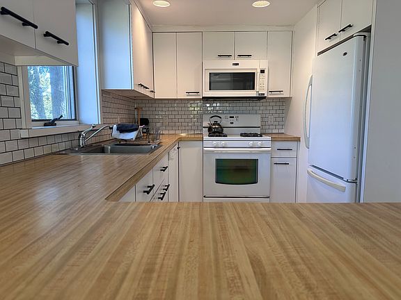 Kitchen featuring white appliances, white cabinetry, and backsplash