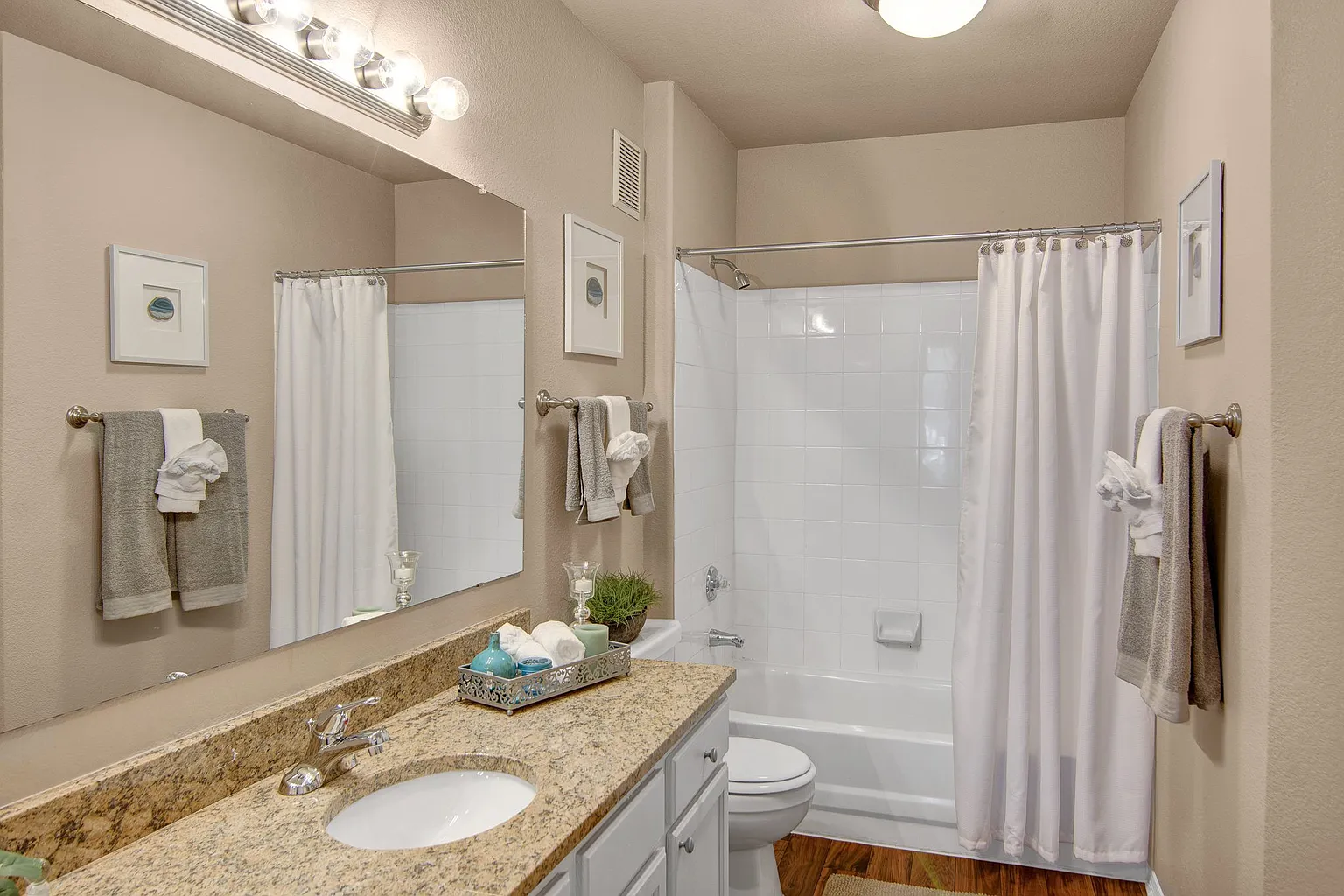 Modern bathroom with granite countertop, vanity, toilet, and bathtub with white tiled shower.