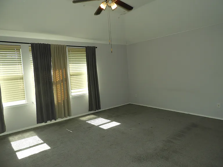 Oversized primary bedroom with large windows, vaulted ceilings and ceiling fan.
