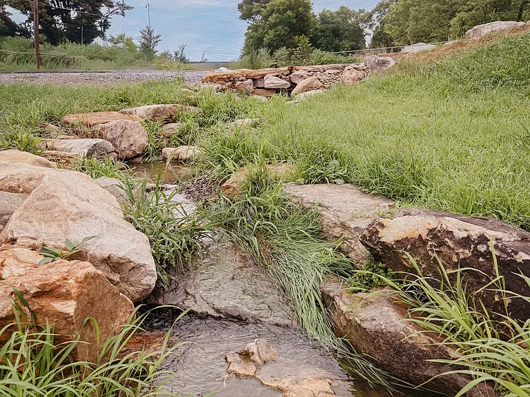 A flowing creek and natural boulders run through the front yard