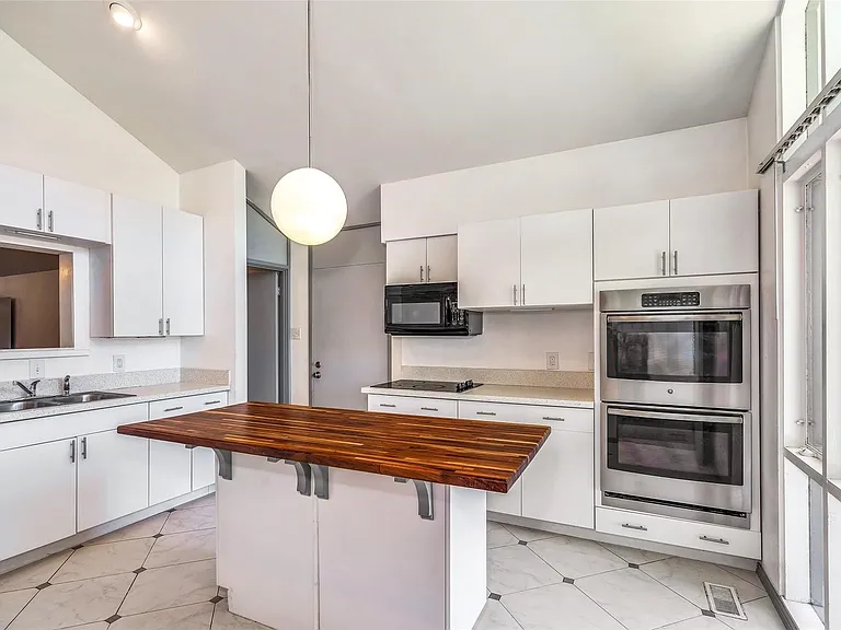 Kitchen featuring a central island with wood-finish countertop, white cabinetry, integrated stainless steel double ovens, and large windows providing natural illumination