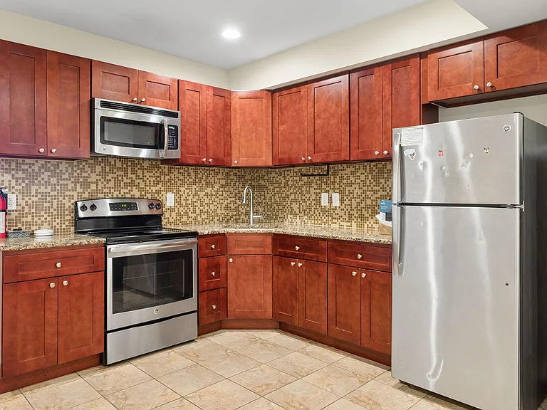 Efficient U-shaped kitchen with ample wood cabinetry, mosaic tile backsplash, and stainless steel range, microwave, and fridg