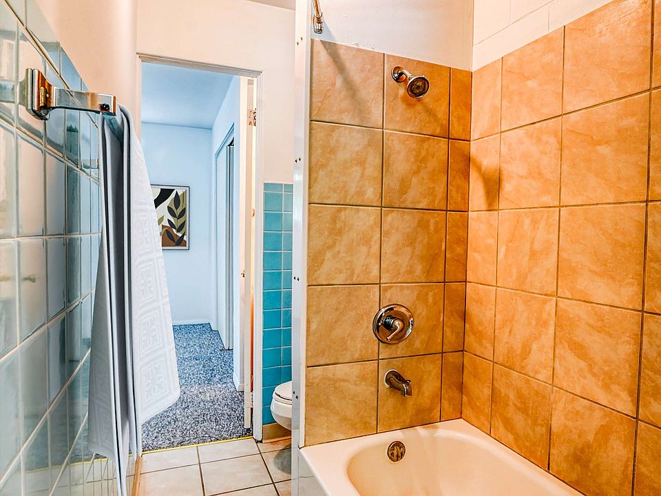 A bathroom with a shower and bathtub, tiled walls, and an open door leading to another room.