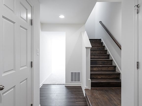Foyer with dark LVP staircase on the right, white walls, and a hallway leading to the finished lower