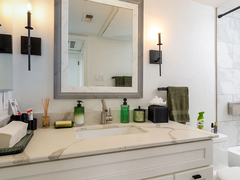 This refreshed bathroom features a sleek vanity with soft lighting and a relaxing shower-tub combo with marble-style tile. Thoughtfully stocked with essentials for a comfortable and easy stay.