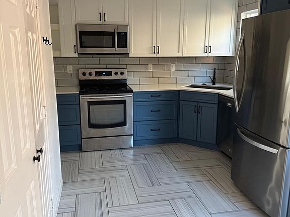 Kitchen featuring two-tone cabinetry with stainless steel appliances, a subway tile backsplash, and herringbone-patterned tile flooring