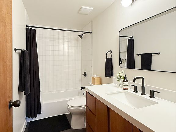 Newly renovated bathroom with solid wood vanity, new tub, matte white tile surround, and black fixtures.