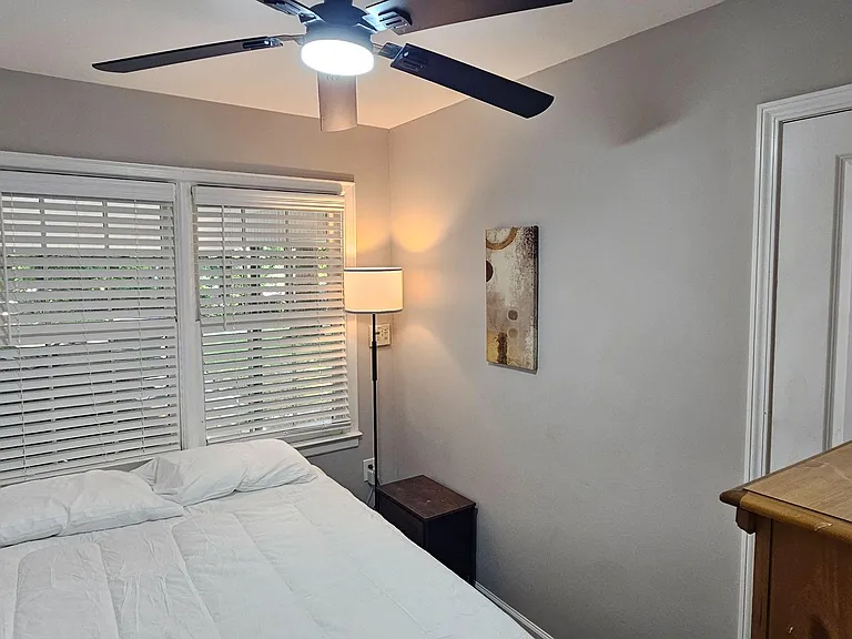 Bedroom with a full bed, large windows with blinds, ceiling fan, and a dresser.