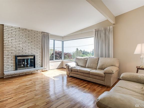 The spacious living room boasts gleaming hardwood floors, vaulted ceilings, a cozy wood burning fireplace and sunny corner windows!