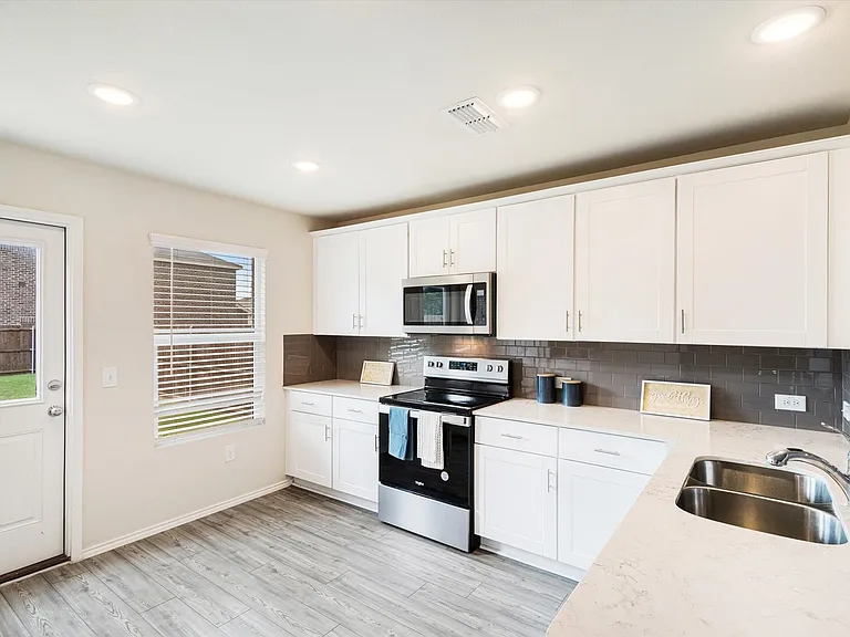 Modern kitchen featuring white cabinetry, light countertops, a stainless steel appliance package, dark subway tile backsplash, and wood-finish flooring