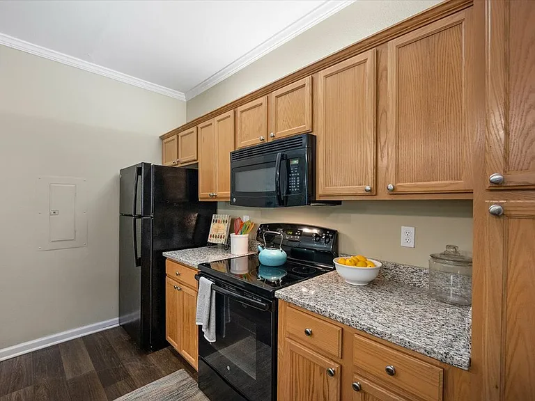 Cook in Style with Granite Countertops, Black Appliances, and Wood Cabinetry at Eagle Flatts Apartments in Hattiesburg
