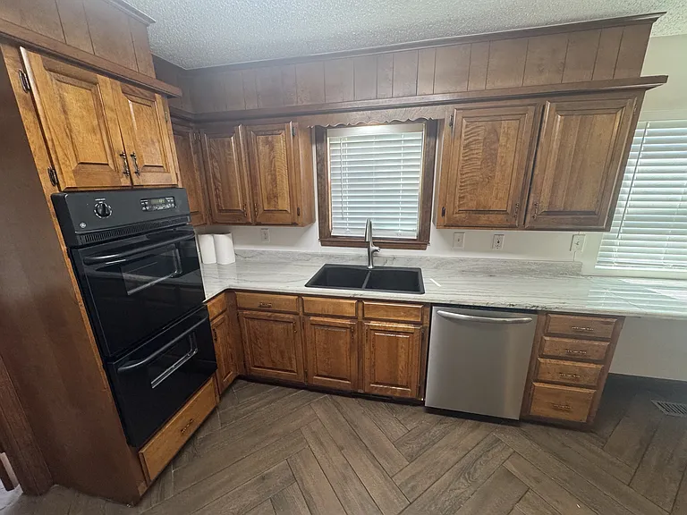 Close up view in kitchen. Double ovens, large double basin sink, dishwasher, and disposal.