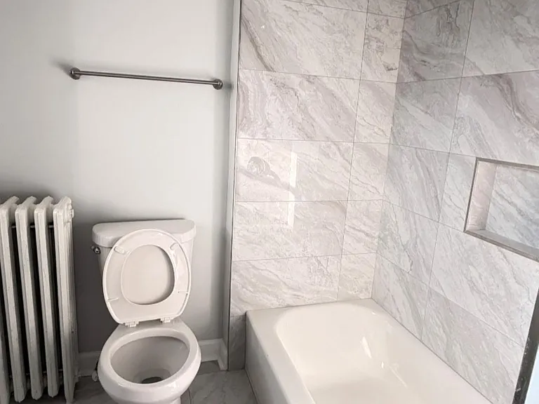 Updated bathroom with a tiled tub/shower surround, built-in shower niche, and matching tile flooring.