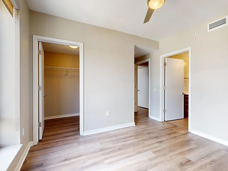 Spacious apartment bedroom with large closet, attached bathroom, and wood-style flooring.
