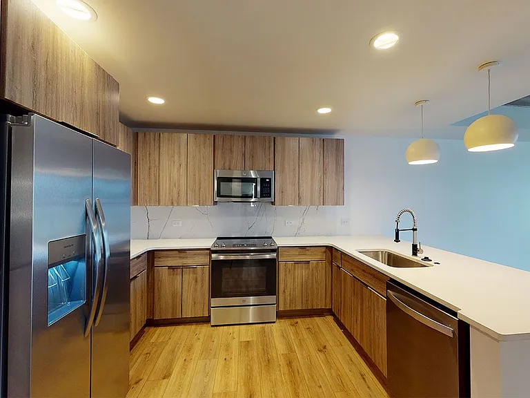 Apartment kitchen with stainless steel appliances, quartz countertops and wood-style flooring.