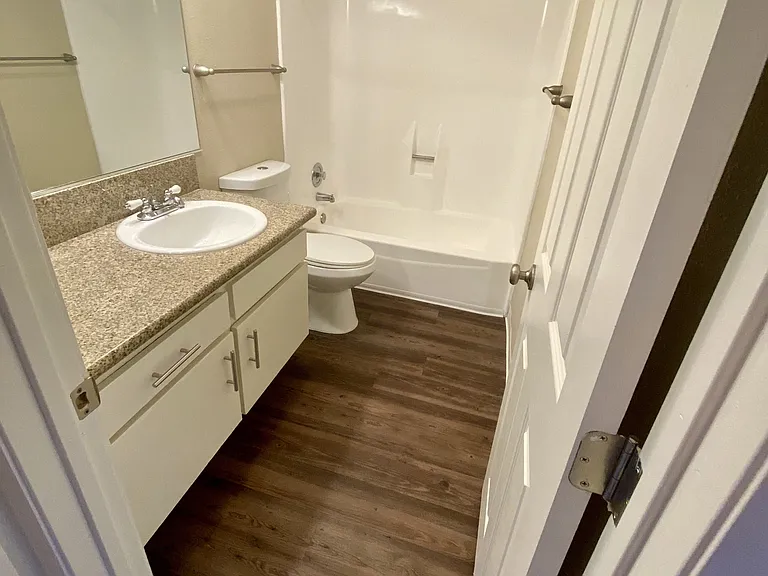 Bathroom with plank style flooring, white vanity cabinets and white fixtures in unit at Villa Pacific Apartments in Oceanside, California.