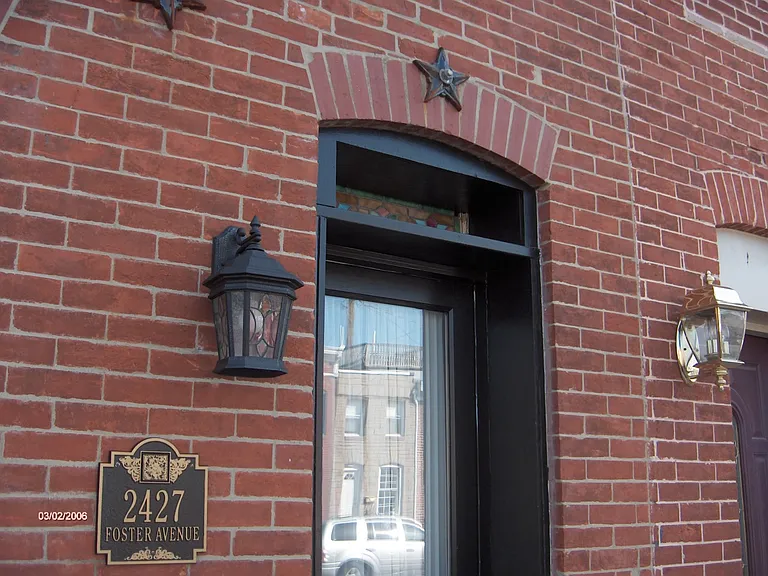 Front door with stained glass transom (above front door) and ornamental ironwork accents at brick facade.