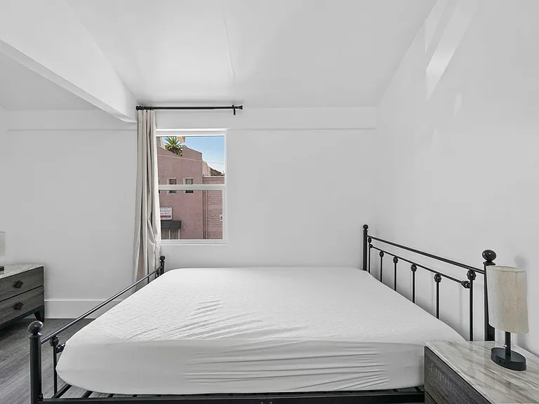 Bedroom with a metal bed frame, nightstands, and a window with curtains providing natural light and outside views.